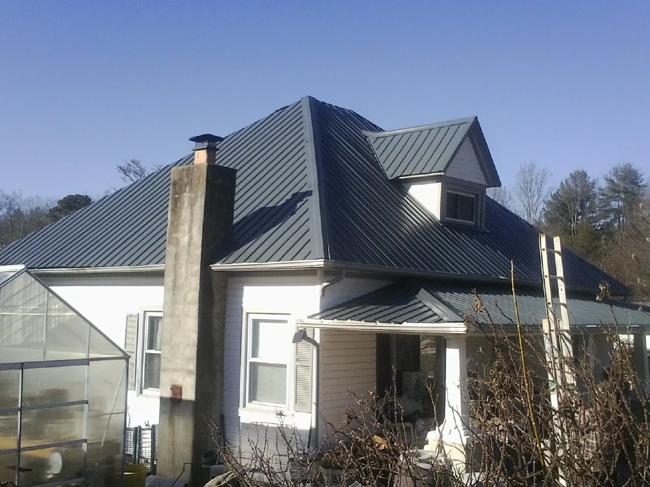 Dark blue standing seam metal roof on a white farmhouse with dormer in Wadesville