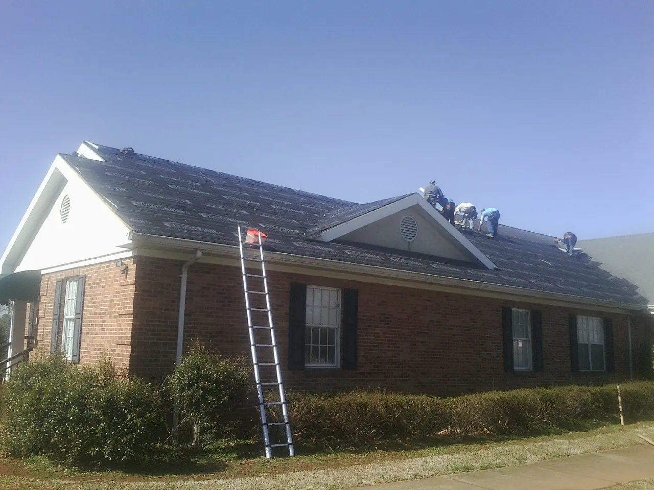 Crew tearing shingles off a brick ranch roof with a ladder set — Metal Roof Repair work by our crew in Wadesville