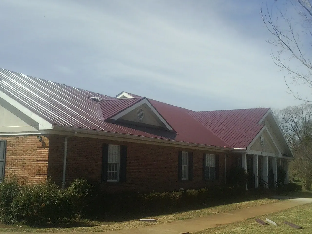 Red metal roof with gabled entries on a long brick building, from a Hail Damage Roof Repair job in Wadesville