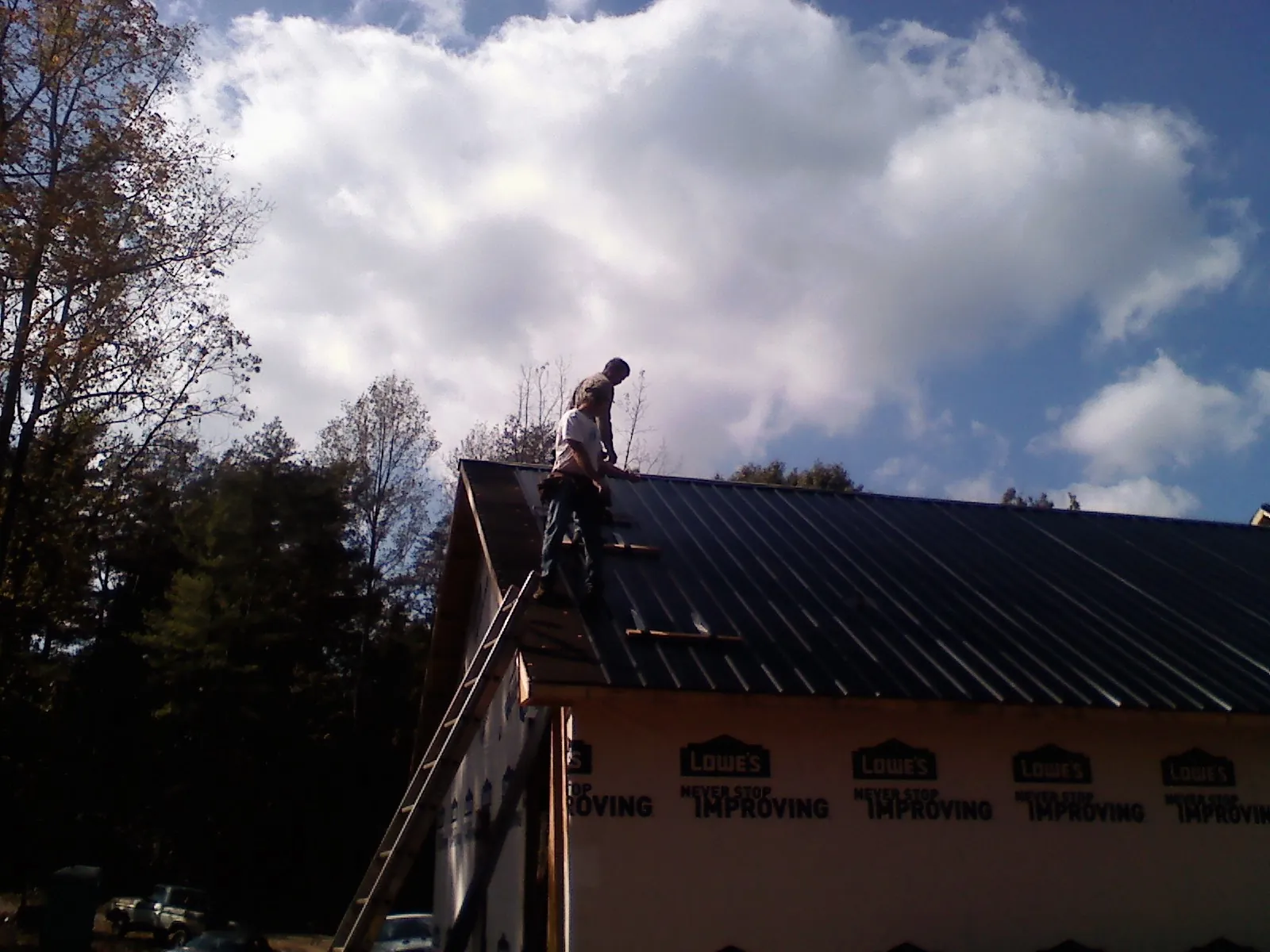 Roofer fastening dark metal panels high against a cloudy sky, from a Roof Inspection job in Wadesville