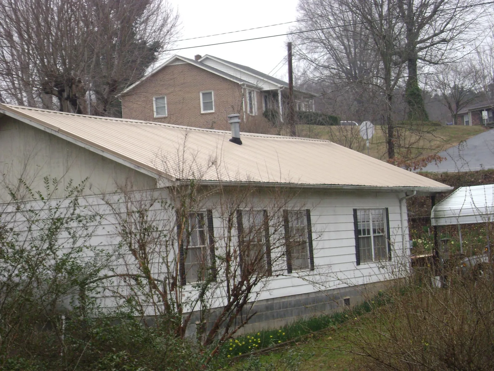 Tan metal roof on a white sided house set into a hillside — Commercial Roofing by Roofing Brothers in Wadesville